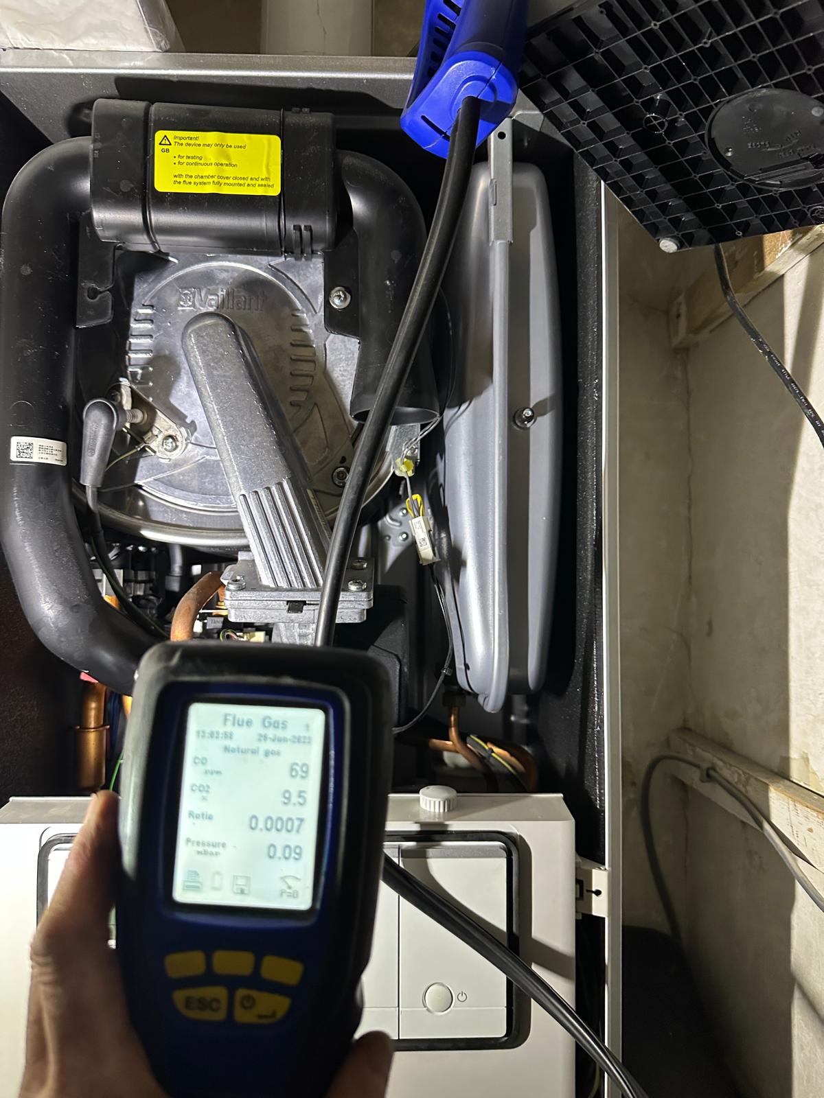 Flue gas analyser held in front of an open Vaillant boiler mid-service