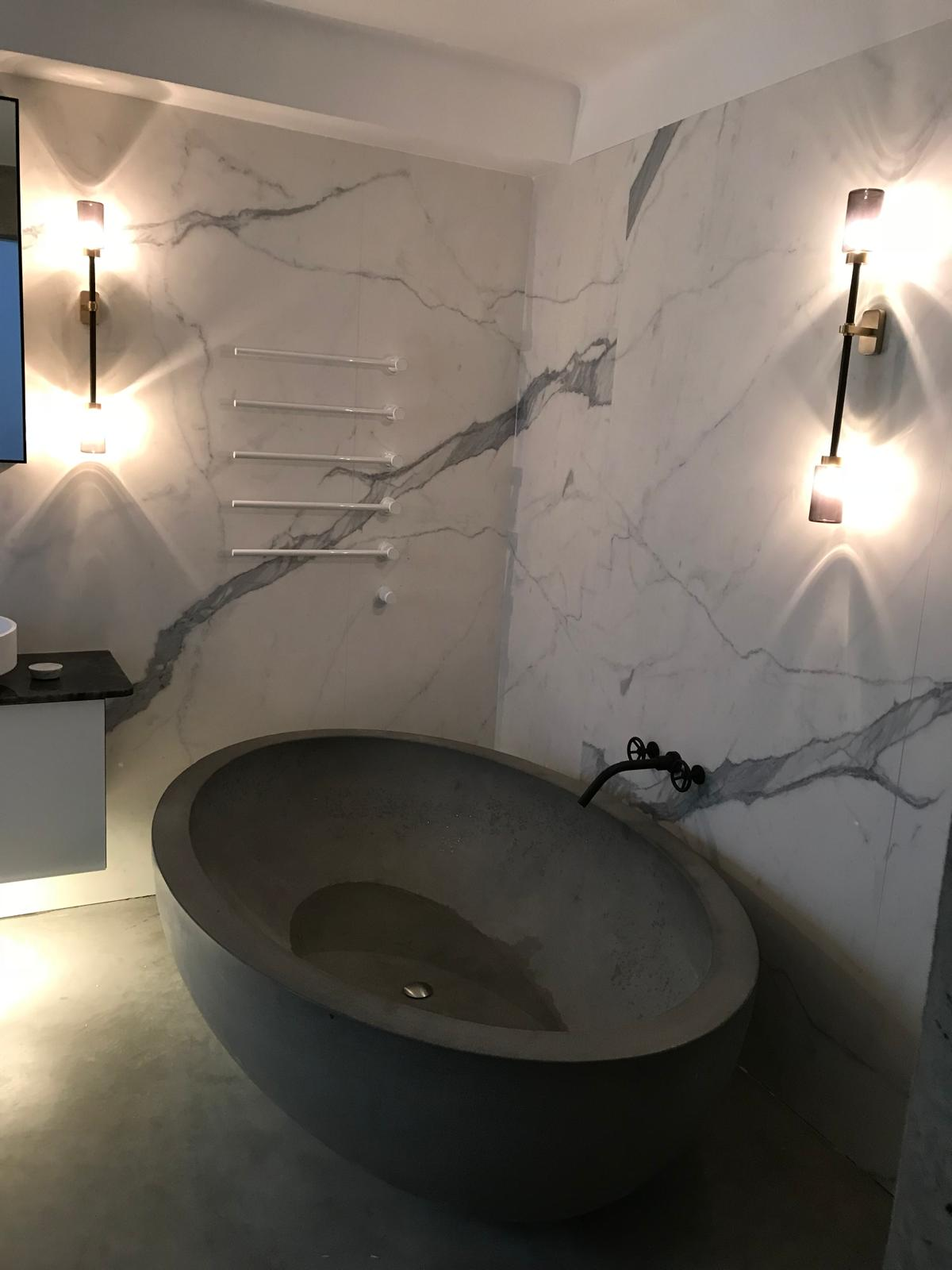 White ladder-style heated towel radiator installed on a full-height marble wall beside a stone freestanding bath — Premier Heating radiator installation